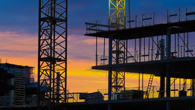 A setting sun with a large-scale construction site in the foreground.