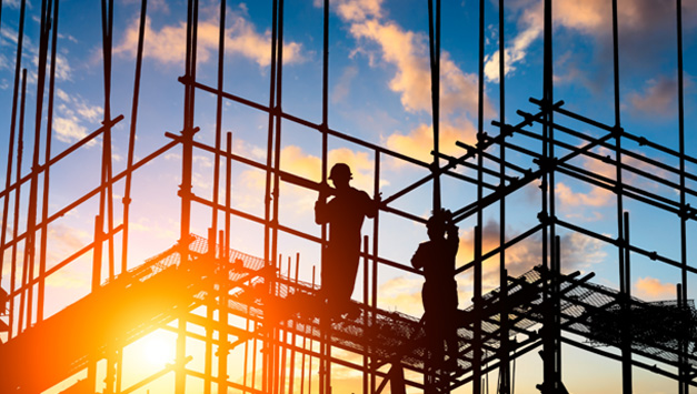 The silhouette of two construction workers on scaffolding, illuminated by a setting sun.