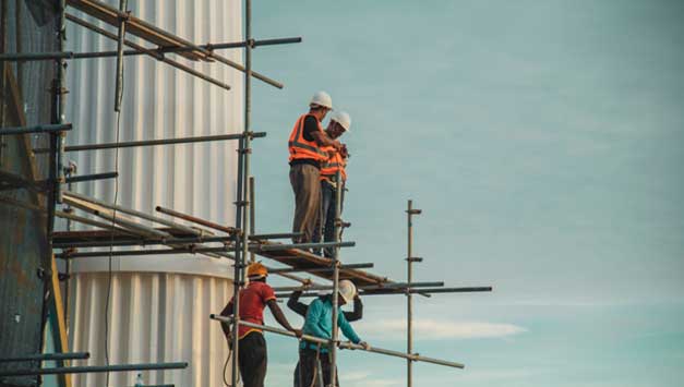 Five construction workers, all wearing hardhats, stand on building scaffolding.