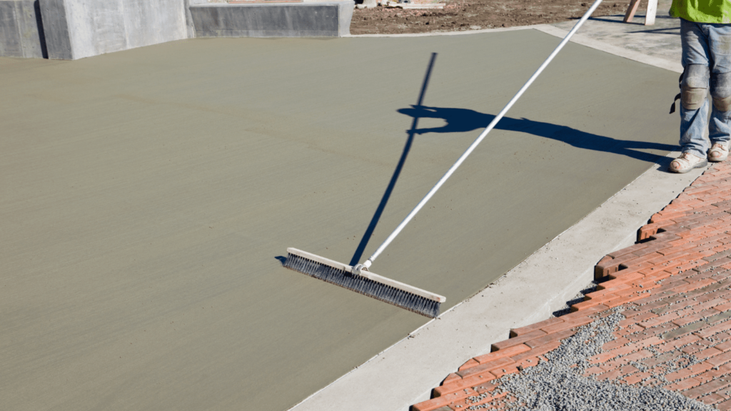 A construction worker uses a long-handled broom to finish concrete.