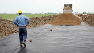 A construction worker walks on geotextile fabric that is being covered by dirt.