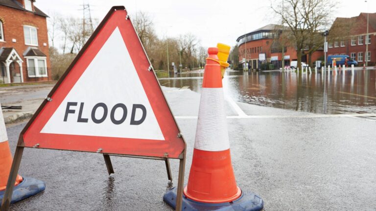 After a heavy rain, a flooded road is labeled with a “flood” construction sign.