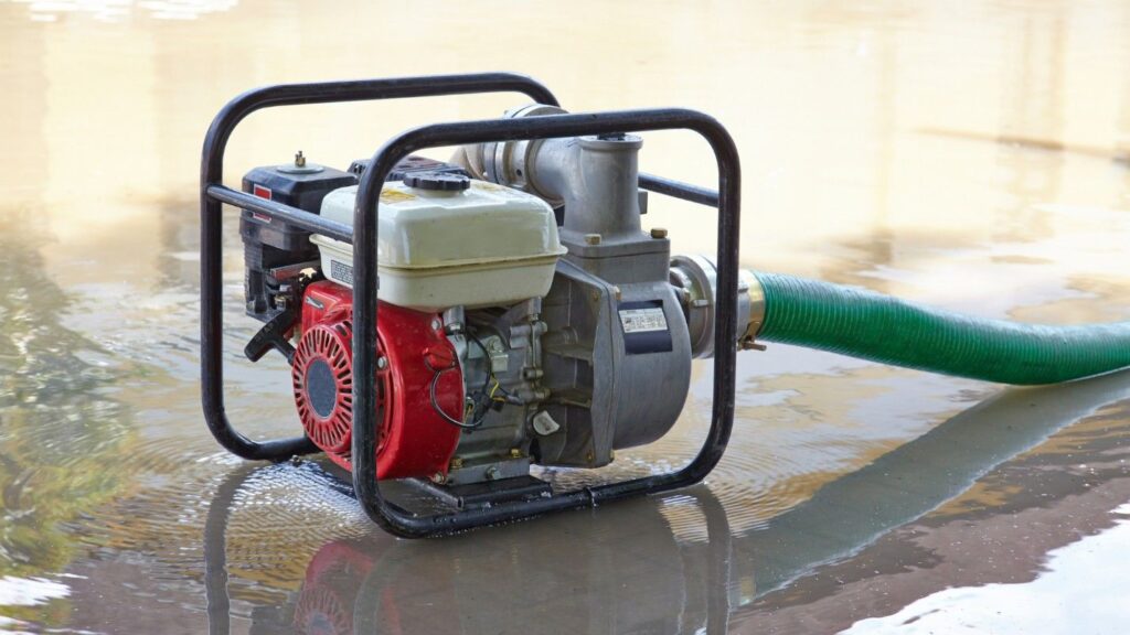 A sump pump generator hooked up to a hose and sitting in a half inch of water.