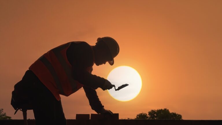 A construction worker places bricks under a hot sun.