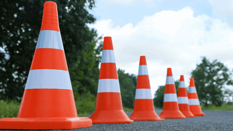 A series of bright orange cones lined up on an asphalt road.