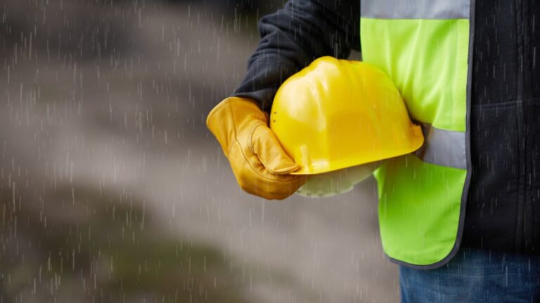 A close-up of a hardhat being held by a construction worker with rain falling.