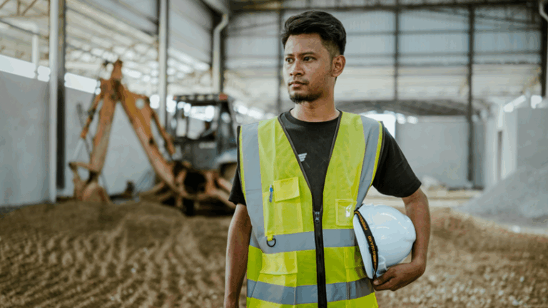 A construction worker holds his hardhat under his arm at a construction site.