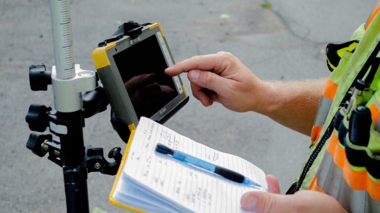 A survey crew member holds a notebook with pencil and presses buttons on a device.