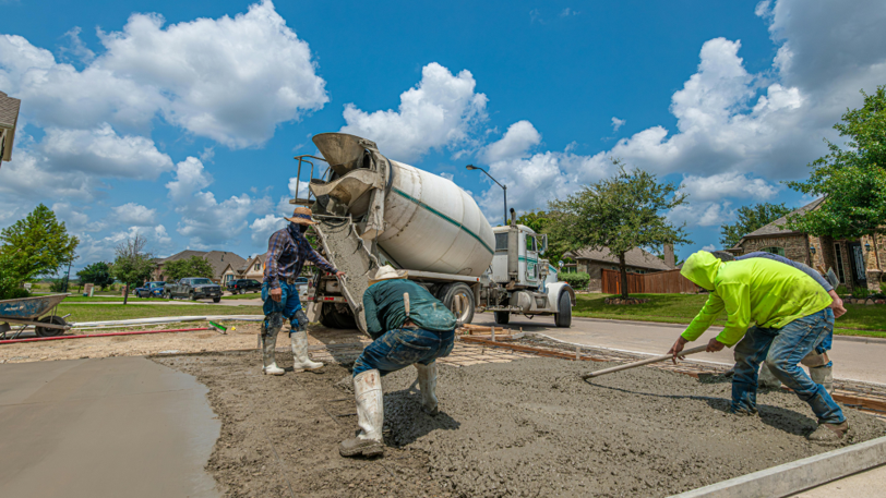 A large truck delivers concrete on site in a residential neighborhood.